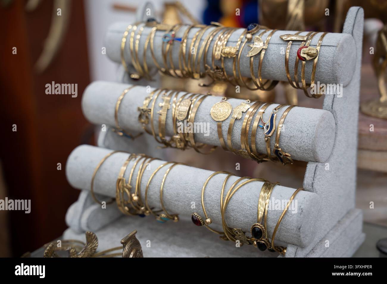 Braccialetti dorati disposti su espositori di velluto grigio in una bottega di souvenir egiziana. Vendita al dettaglio di gioielli e commercio locale. Foto Stock