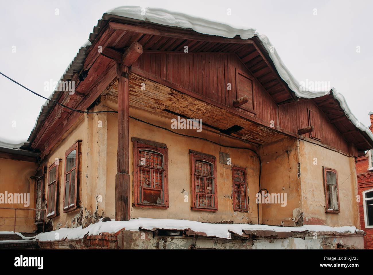 Vecchia casa di legno fatiscente con pareti danneggiate e tetto coperto di neve in inverno Foto Stock