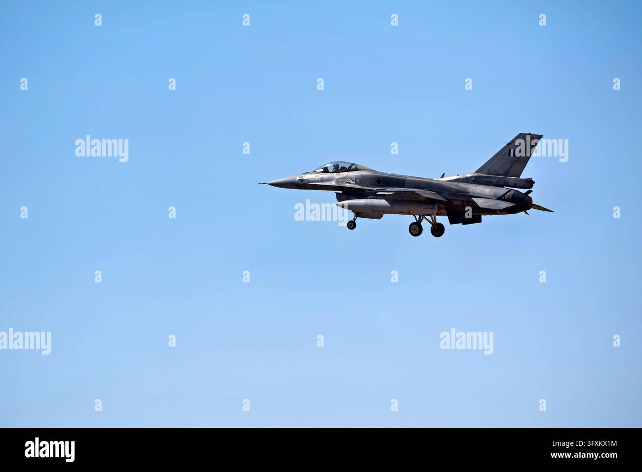 Jet da combattimento militare con il carrello di atterraggio esteso si avvicina per atterrare contro un cielo blu chiaro durante una missione di volo Foto Stock