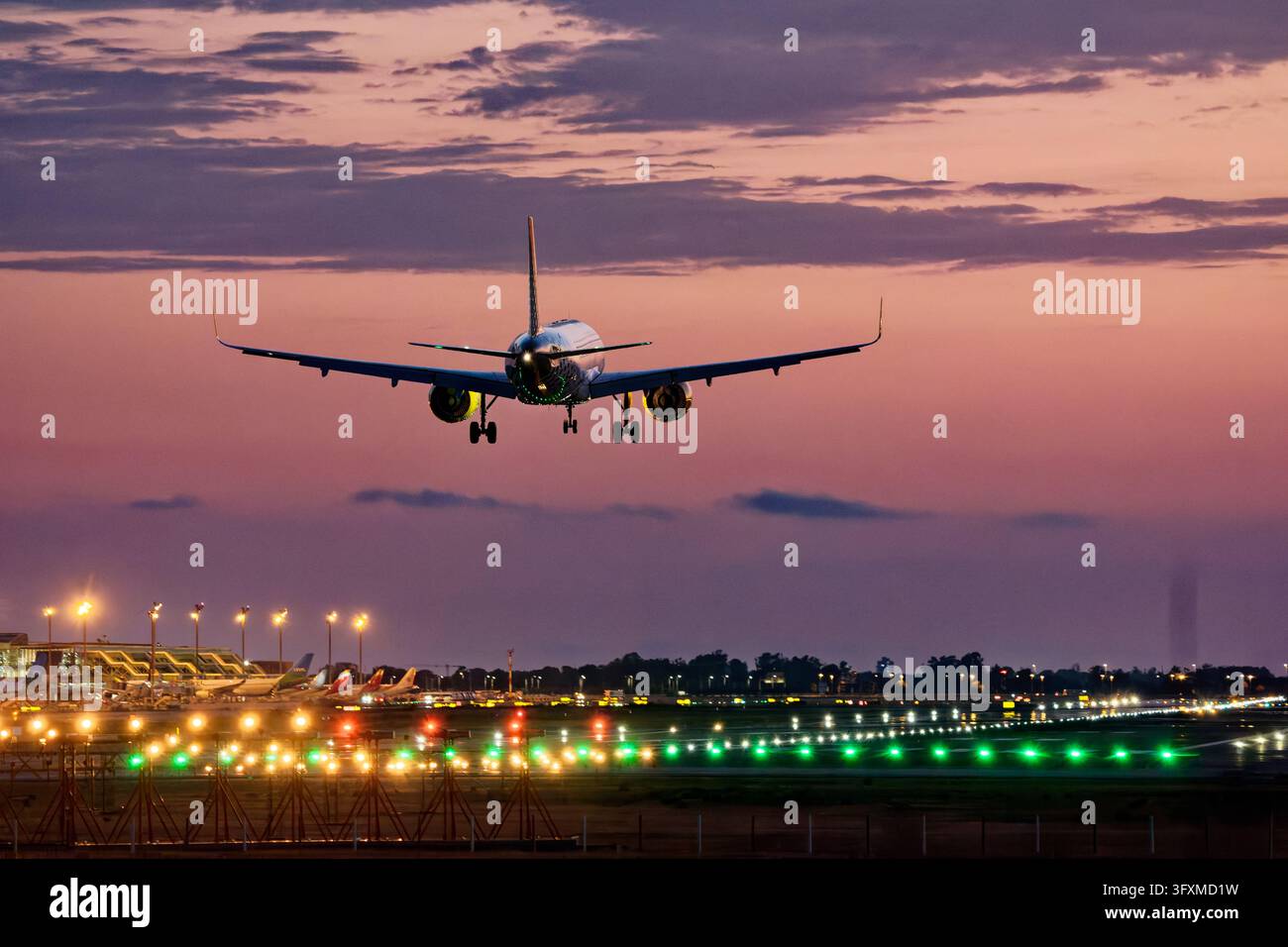 Aereo che atterra sulla pista al tramonto con le luci dell'aeroporto Foto Stock