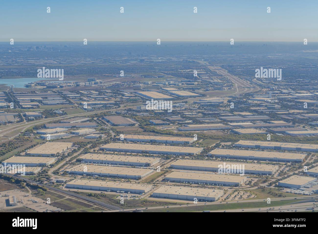 Vista aerea di un vasto parco industriale con numerosi grandi magazzini, centri di distribuzione e infrastrutture autostradali sotto un cielo sereno. Foto Stock