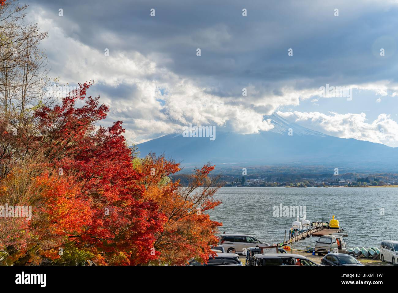 Il Monte Fuji si erge in lontananza dietro il lago Kawaguchiko, incorniciato da vibranti aceri rossi e arancioni in primo piano. Foto Stock