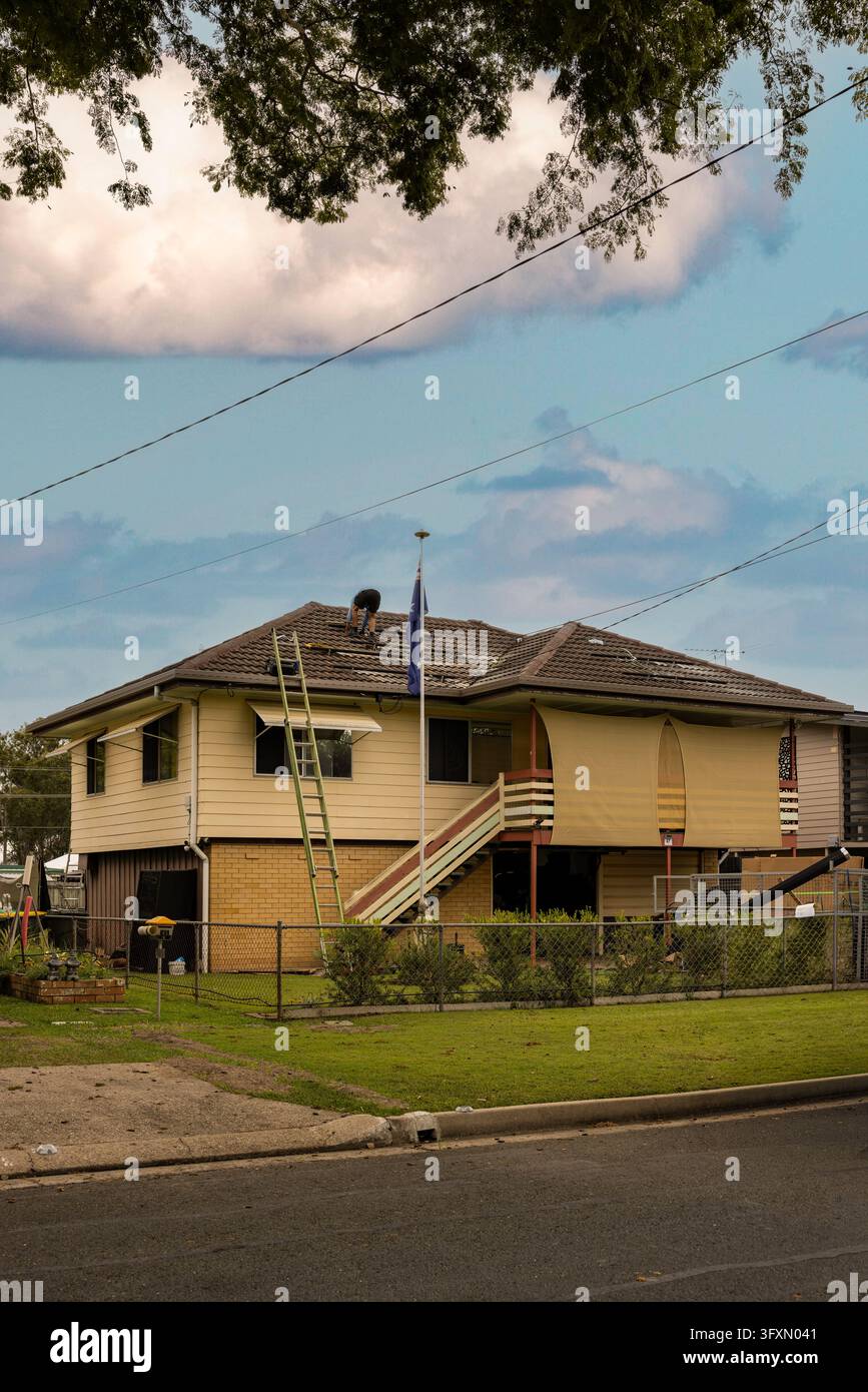 uomo tetto casa mani sotto barra piegato in avanti faccia verso il basso installazione telai pannelli solari Queensland Australia immagine paesaggio orizzontale Foto Stock
