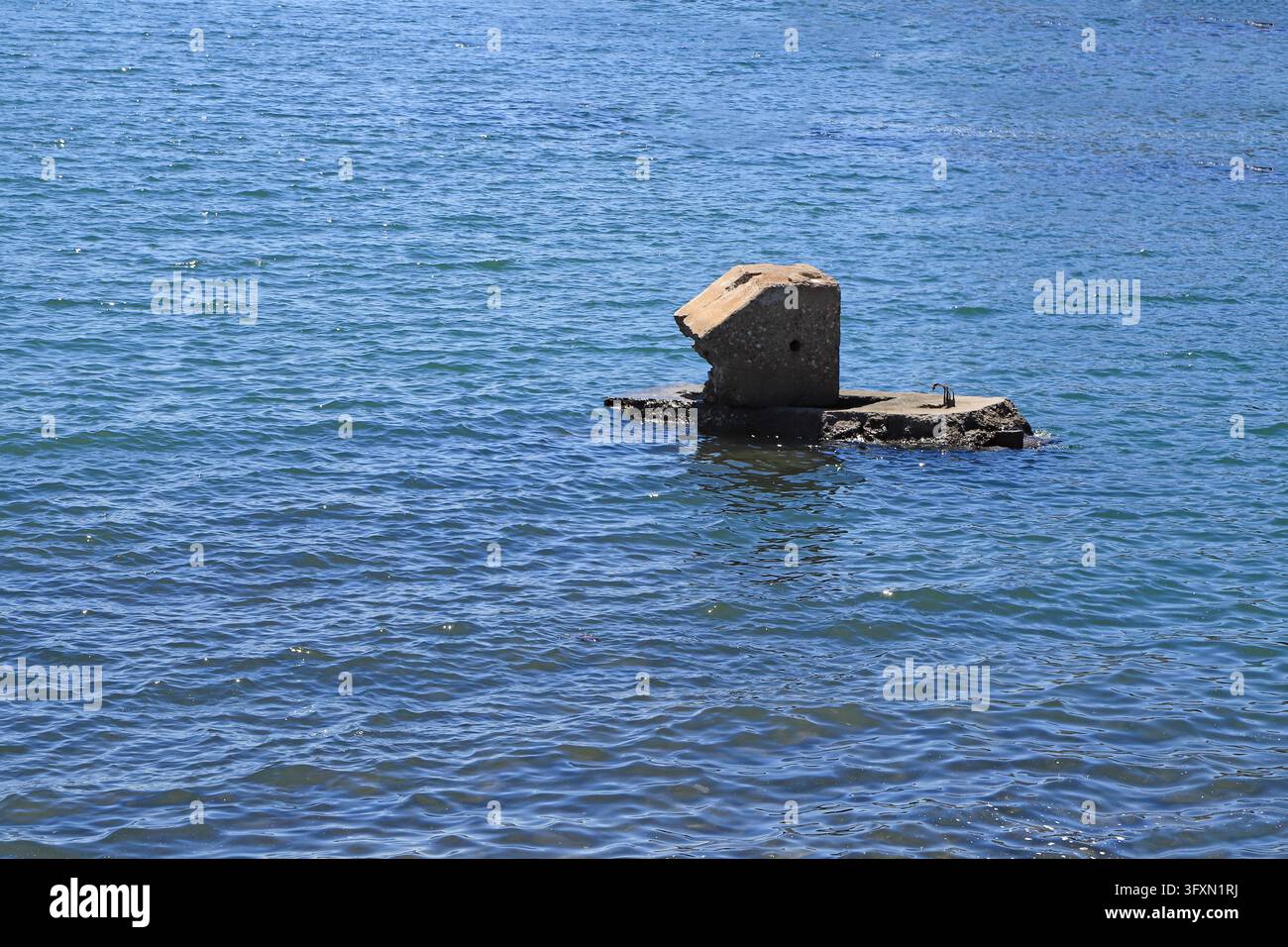 Fondazione di molo in cemento abbandonata e danneggiata emerge sopra l'acqua blu, struttura portuale antica rimasta, quieto paesaggio industriale costiero del patrimonio. Foto Stock