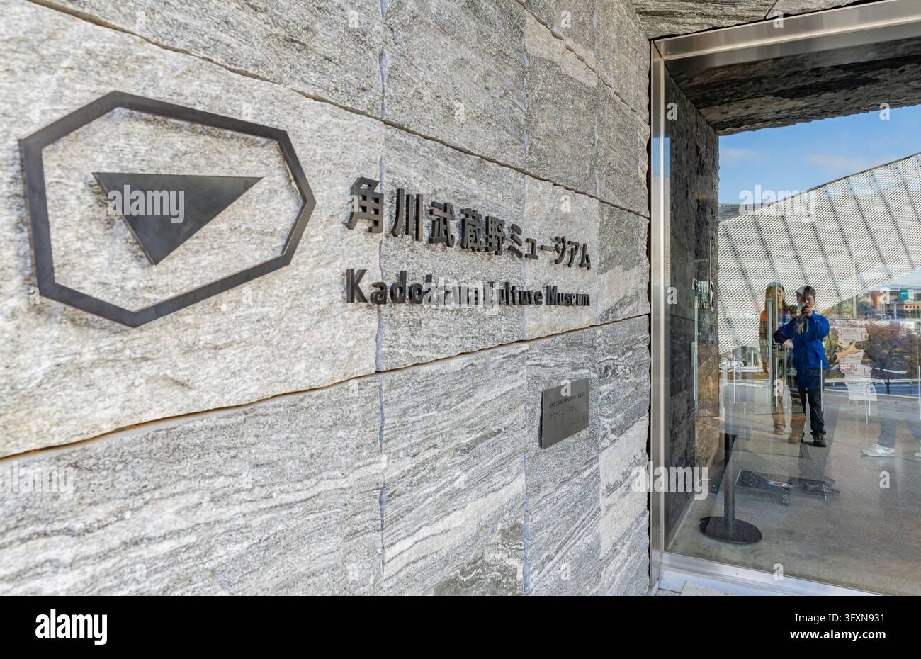 Tokyo, Giappone, 22 NOV 2024 - Primo piano del logo e del nome del Museo della Cultura Kadokawa su un muro di pietra strutturato, con un ingresso in vetro che riflette un visitatore Foto Stock