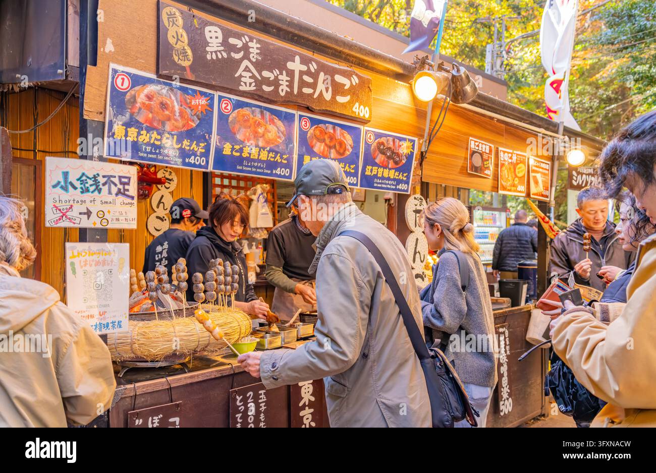 Tokyo, Giappone, 22 NOV 2024 – Le persone si radunano a un chiosco di cibo da strada in legno a Hachioji, Tokyo, acquistando spiedini di dango esposti su un banco di paglia. Foto Stock