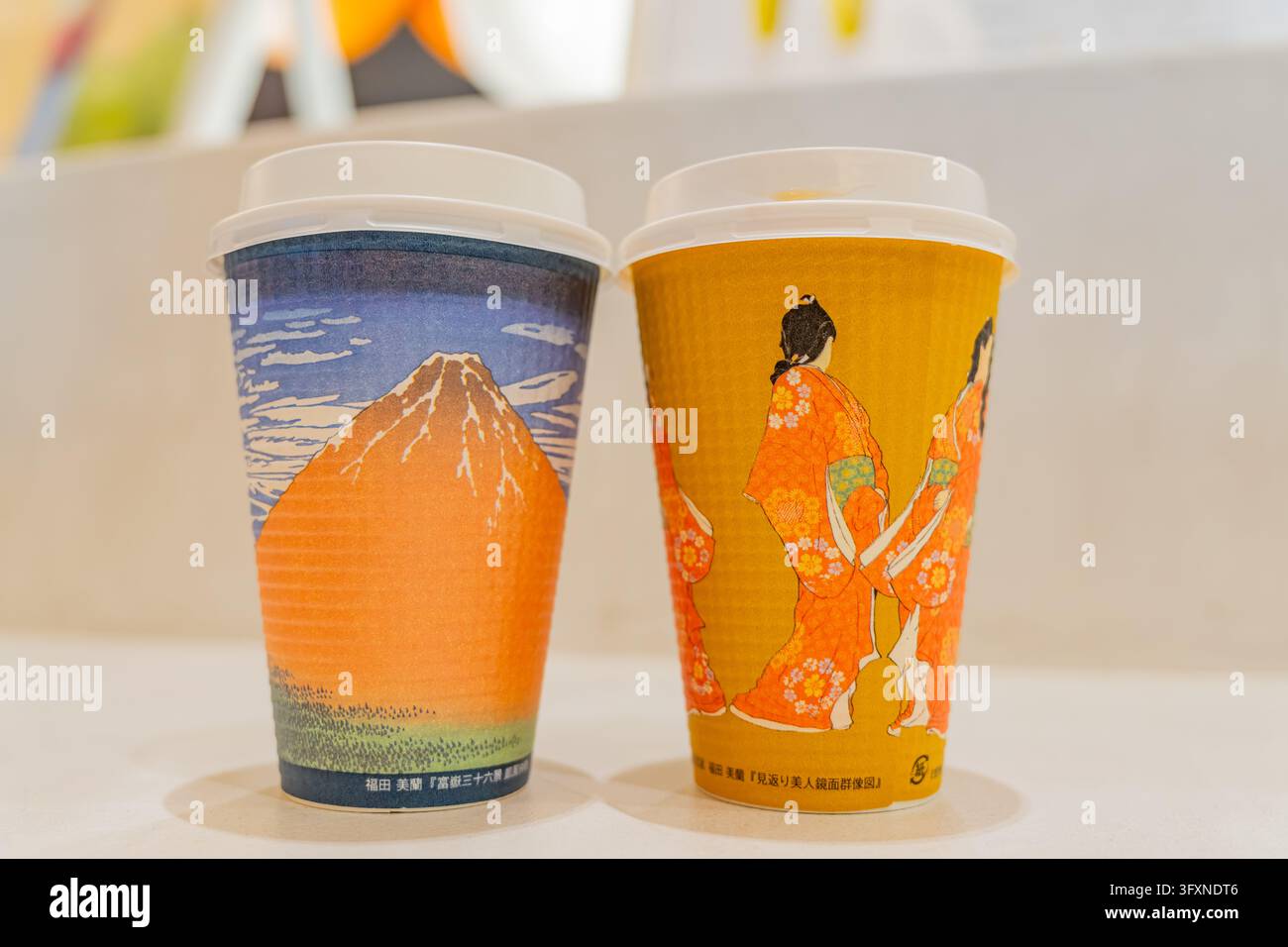 Tokyo, Giappone, 22 NOV 2024 - Due bicchieri di carta monouso con coperchi bianchi appoggiati su una superficie bianca, decorati con stampe giapponesi ukiyo-e del Monte Fuji an Foto Stock