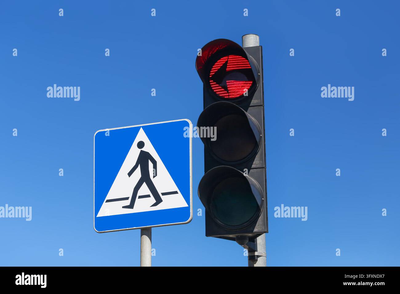 Semaforo pedonale rosso accanto a un cartello di attraversamento pedonale blu su un cielo sereno. Sicurezza stradale urbana, normative sul traffico e infrastrutture stradali. Foto Stock