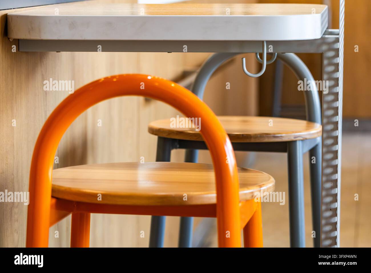 Sgabelli da bar moderni con strutture tubolari arancioni e grigie sono posizionati sotto un bancone bianco con un gancio attaccato in uno spazio da pranzo interno. Foto Stock