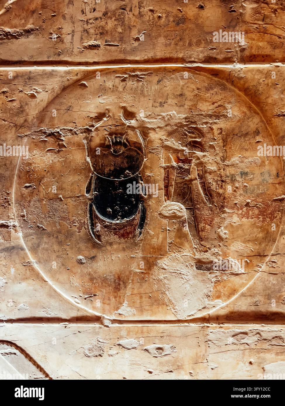 LUXOR, EGITTO – 12 aprile 2026: Antico rilievo dipinto di uno scarabeo e di un disco solare intagliato in una parete di arenaria. Foto Stock
