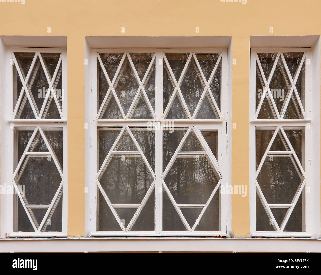 Finestre vintage con cornici di legno bianco creano motivi a rombo e triangolari nelle lastre riflettenti inserite in una parete gialla calda su una vecchia facciata Foto Stock