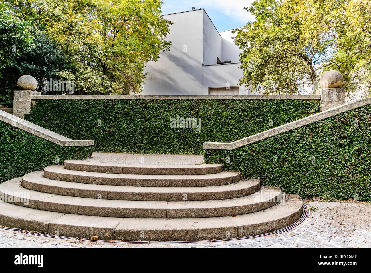 Una scala semicircolare in pietra naturale conduce a un muro di sostegno densamente ricoperto di vegetazione nel parco della Fundação de Serralves (Fondazione Serralves) a Porto, Portogallo. Su dei pali delle ringhiere si trovano sfere di pietra. Dietro, si innalza una parte del Museu de Arte Contemporânea de Serralves. Álvaro Siza Vieira ha progettato il museo. È stato inaugurato il 6 giugno 1999. Foto Stock
