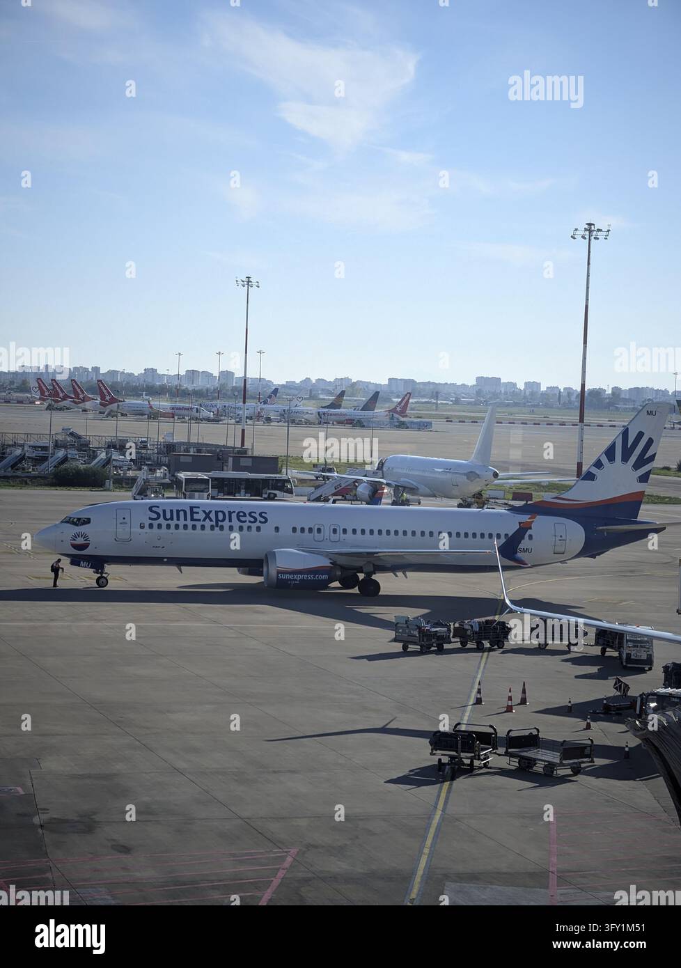 Aereo di linea sulla pista dell'aeroporto illuminata dal sole con attrezzature di terra e skyline cittadina in lontananza Foto Stock
