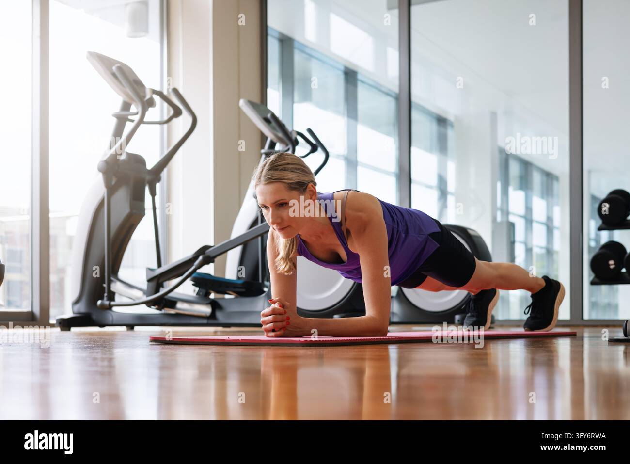 Donna atletica che esegue l'esercizio del plank su un tappeto da fitness in palestra Foto Stock
