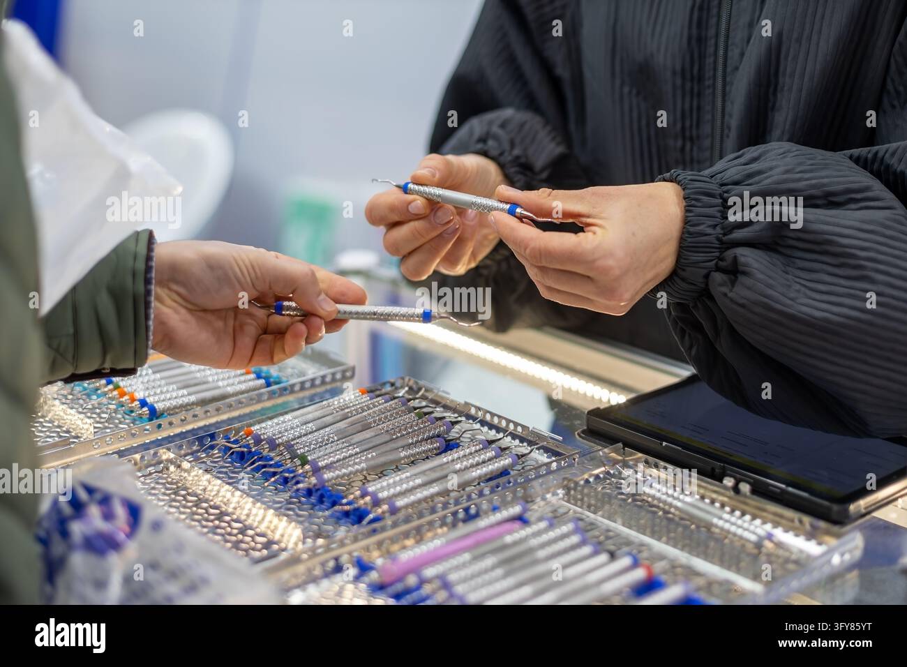 Professionisti dentali che esaminano strumenti dentali in acciaio inossidabile a una fiera di attrezzature mediche, primo piano di mani che confrontano strumenti di precisione per Foto Stock