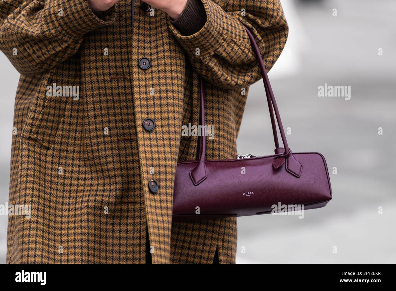 Parigi, Francia - 11 marzo 2025: Donna indossa una borsa a tracolla in pelle bordeaux Alaia Le Teckel con cappotto a quadri Foto Stock