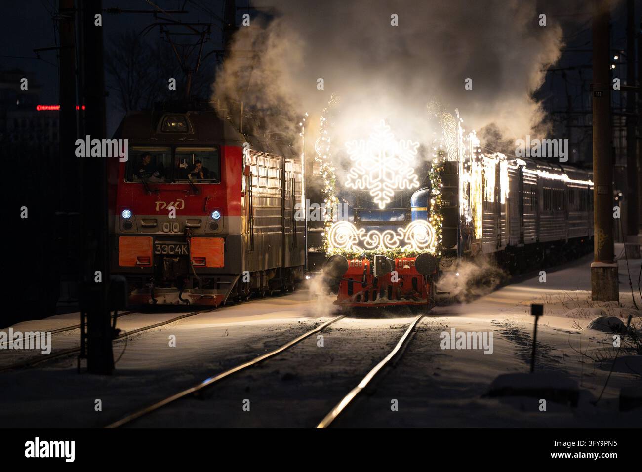 L'equipaggio di una locomotiva elettrica filma un treno a vapore natalizio che passa su una ferrovia innevata durante una mattina d'inverno Foto Stock