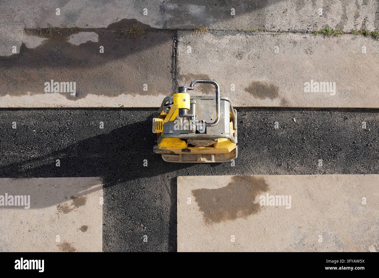 Vista aerea di un compattatore a piastra vibrante posizionato su una trincea di asfalto fresco durante i lavori di costruzione stradale Foto Stock
