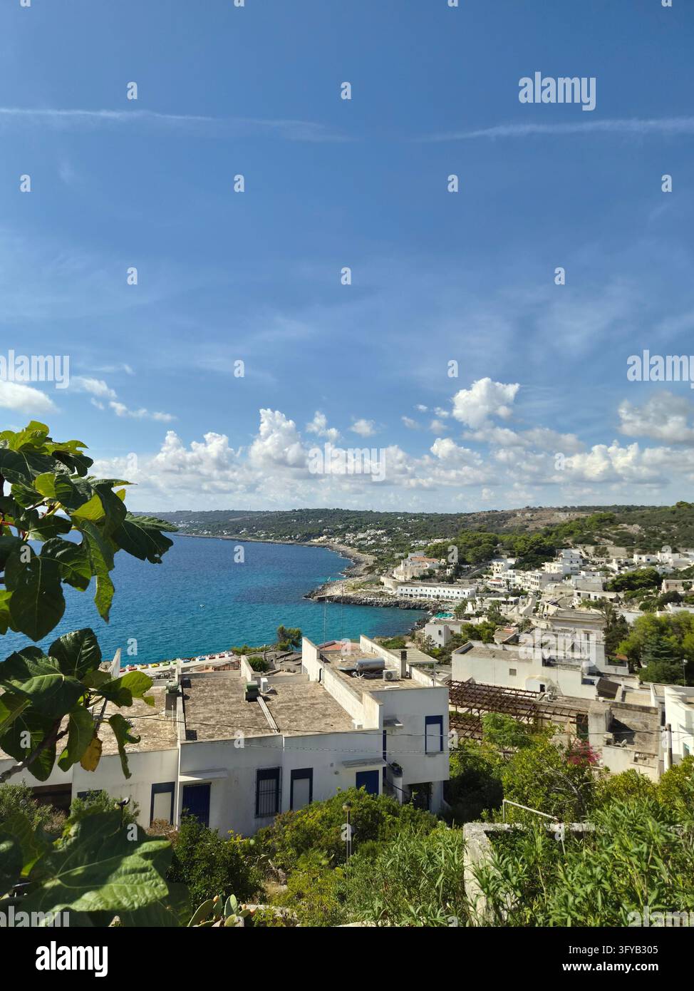 Città di Castro Marina e baia sulla costa adriatica viste attraverso foglie di fico, case bianche sul pendio sotto le nuvole estive, Castro, Salento, Puglia, Italia, settembre 2026 - Immagine stock catturata con smartphone