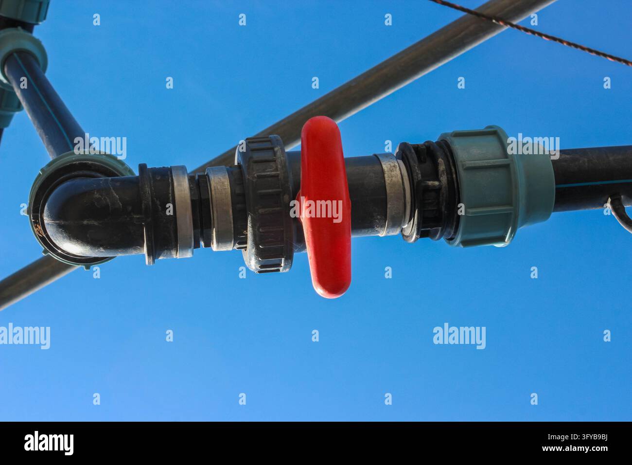 Un tubo di plastica nero con una maniglia della valvola rossa impostata in posizione chiusa su un cielo blu chiaro. Foto Stock