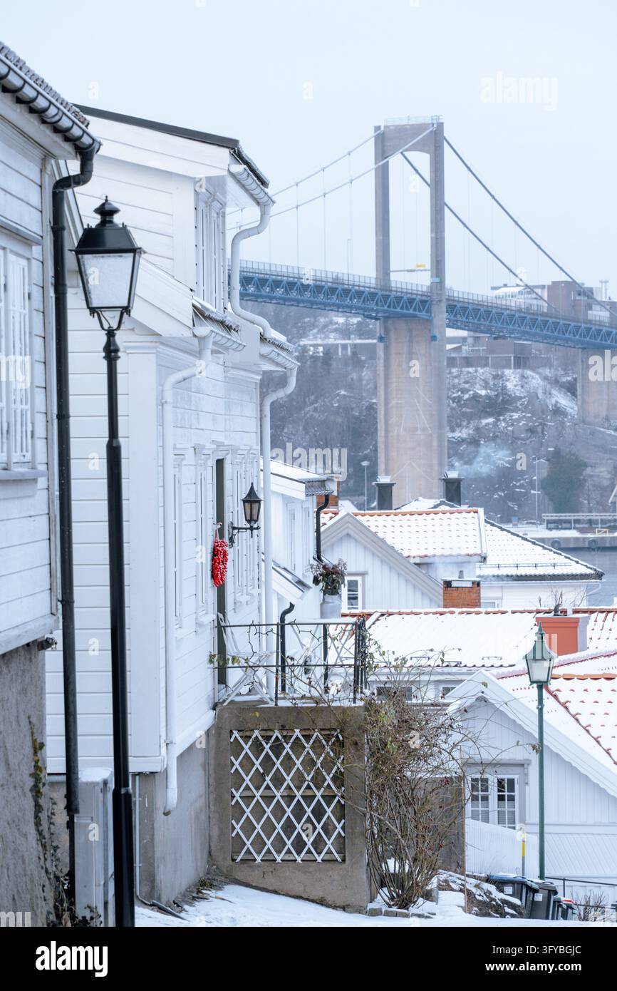Via del patrimonio sotto collegamenti infrastrutturali case di legno bianche e lampade tradizionali con un grande ponte sospeso oltre i tetti coperti di neve in una N Foto Stock