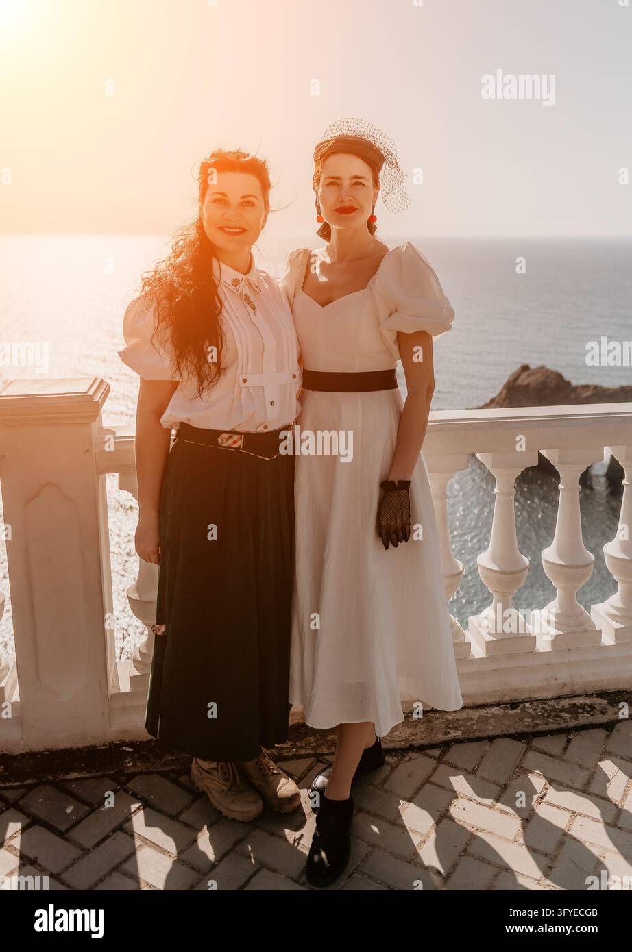 Moda vintage femminile in posa su un balcone bianco affacciato sul mare durante il tramonto per un ritratto mediterraneo classico Foto Stock