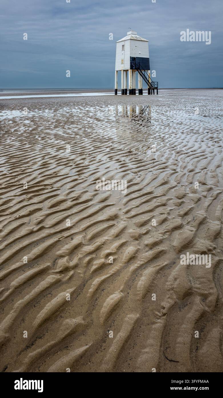 Inghilterra, Somerset, Burnham on Sea. Un faro bianco rialzato si erge sopra la sabbia bagnata e increspata durante la bassa marea, con pozze poco profonde che riflettono le sue gambe sottostanti Foto Stock