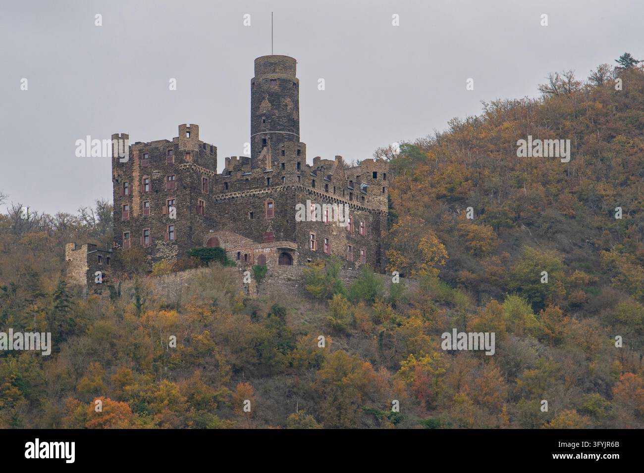 Castello di pietra medievale con torri merlate che si ergono sopra una collina boscosa autunnale Foto Stock