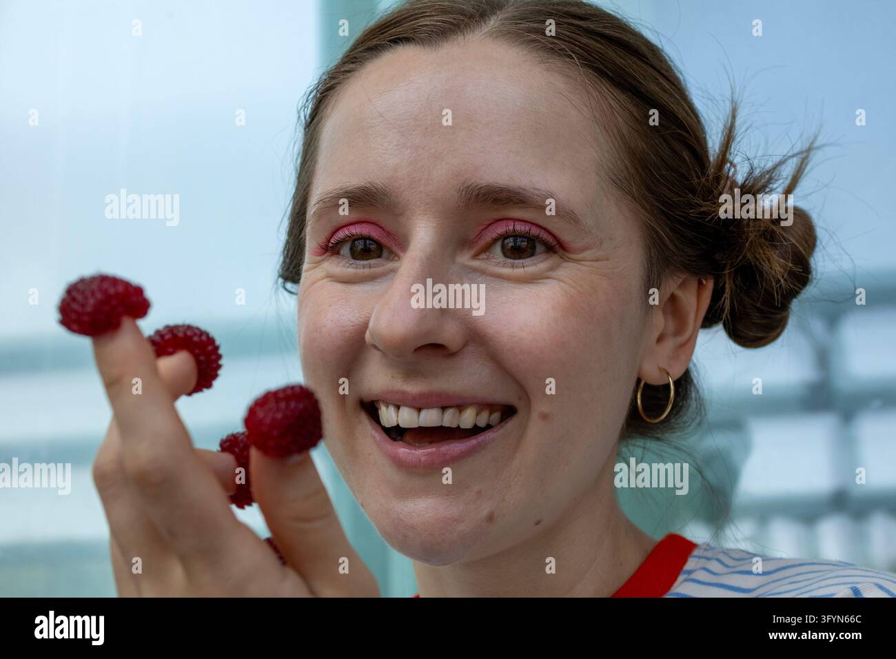Giovane donna sorridente che tiene giocosamente lamponi freschi sulle punte delle dita Foto Stock