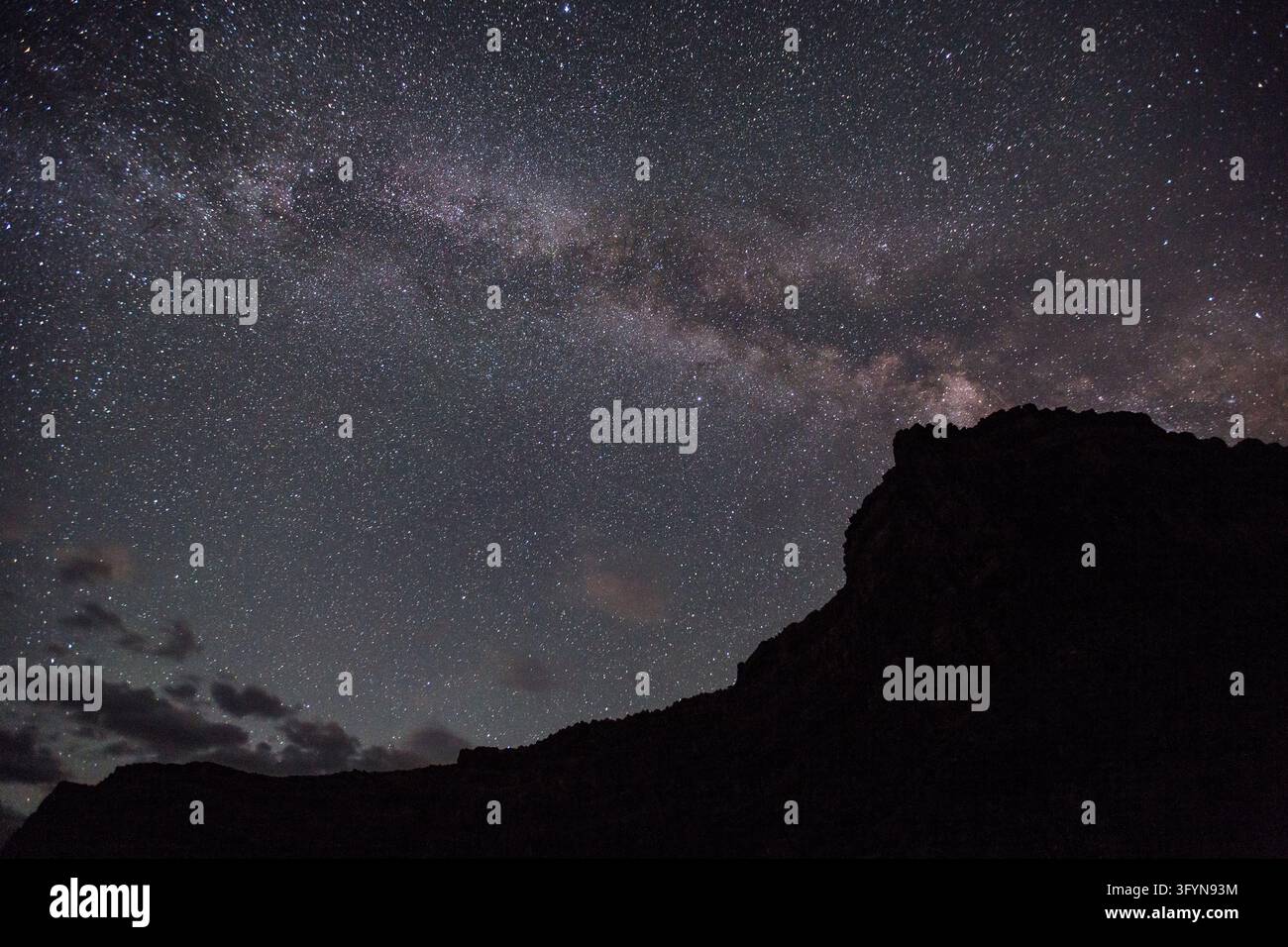 Una fotografia a lunga esposizione che cattura la Via Lattea che si estende nel cielo notturno sopra Anderson Hole nel Dinosaur National Monument, USA. La banda luminosa di stelle e polvere cosmica divide la cupola celeste oscura sopra la silhouette prominente di un butte di arenaria, con nuvole sparse che fluttuano vicino all'orizzonte inferiore. Il paesaggio notturno dimostra i cieli eccezionalmente scuri e l'atmosfera stellare naturale preservati nella regione protetta dei canyon dell'Ovest americano. Una versione ottimizzata di un'immagine del US National Park Service. Credit: NPS / J Frank Foto Stock