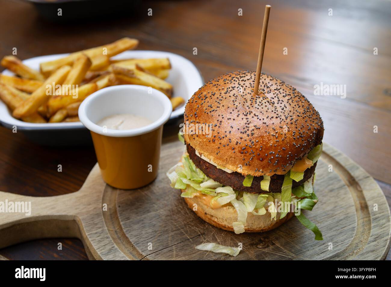hamburger vegetariano con una polpetta a base di piante servito con patatine fritte croccanti e salsa da intingere su un vassoio di servizio in legno Foto Stock