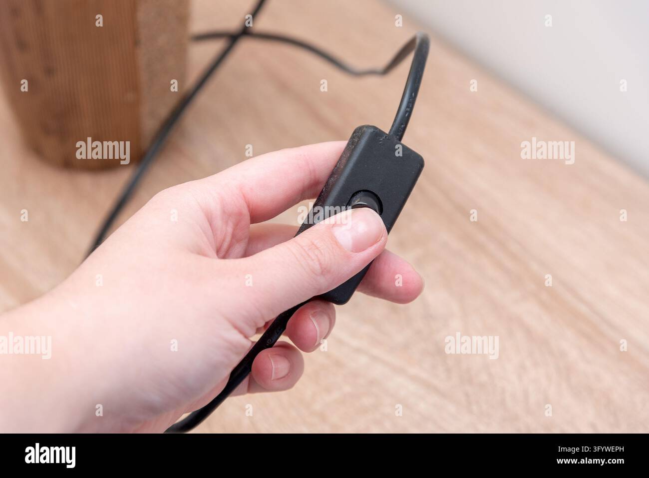 Mano preme un pulsante su un interruttore a cavo nero in linea, che controlla un dispositivo elettrico domestico. Una vista ravvicinata mostra le dita che tengono l'interruttore cablato sopra una luce Foto Stock