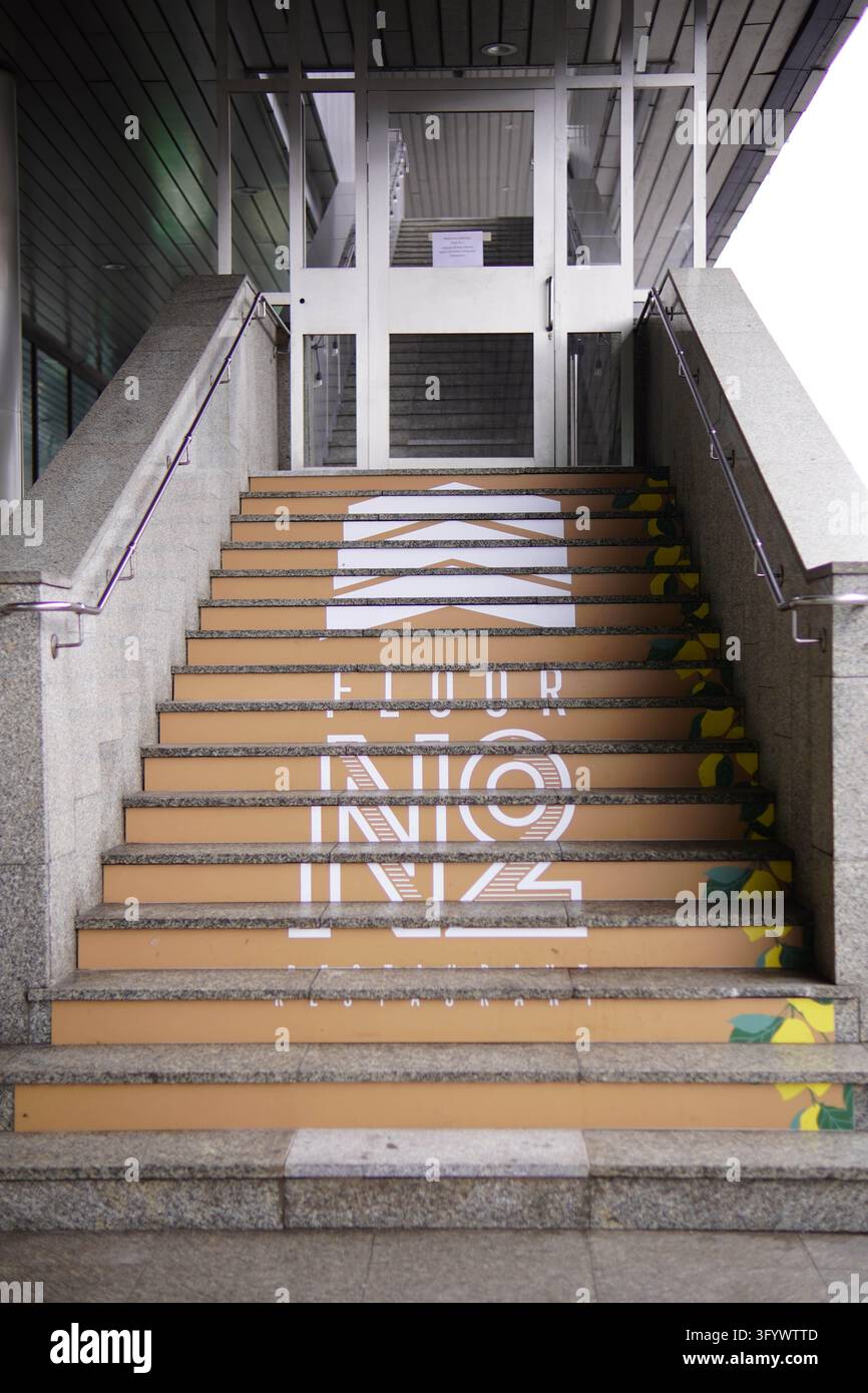 Varsavia, Polonia - 28 ottobre 2026: Scritte dipinte e accenti geometrici decorano le scale esterne sotto una struttura d'ingresso in vetro e metallo Foto Stock