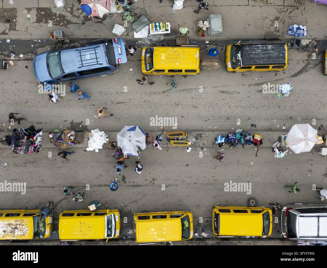 Vista aerea di una strada trafficata a Lagos con minibus gialli, auto parcheggiate e persone che camminano tra le bancarelle del mercato con ombrelli a Lagos, Lagos Foto Stock