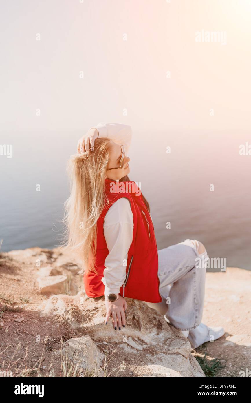 Donna su una scogliera oceanica seduta su una sporgenza rocciosa che si affaccia sull'acqua calma durante il tramonto con ampio spazio per il testo Foto Stock