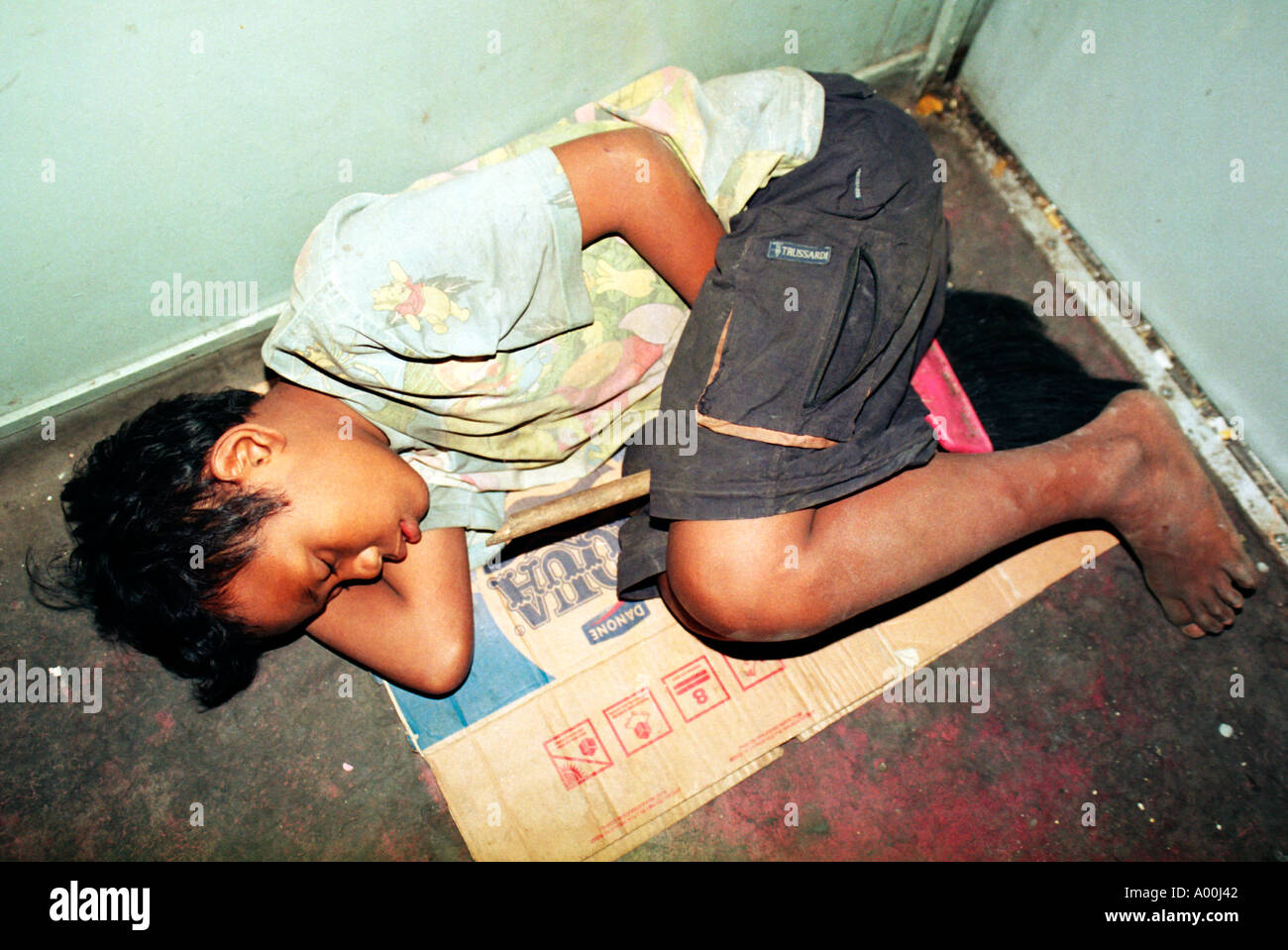 Grubby giovani senzatetto ragazzo dorme sul cartone in uno dei treni che spazza il pennello pulito in modo sicuro tra le sue gambe east java Foto Stock
