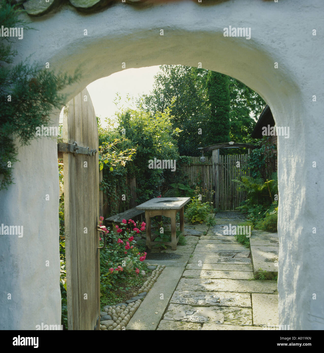 Vista attraverso il giardino aperto porta nella parete al cortile pavimentato Foto Stock