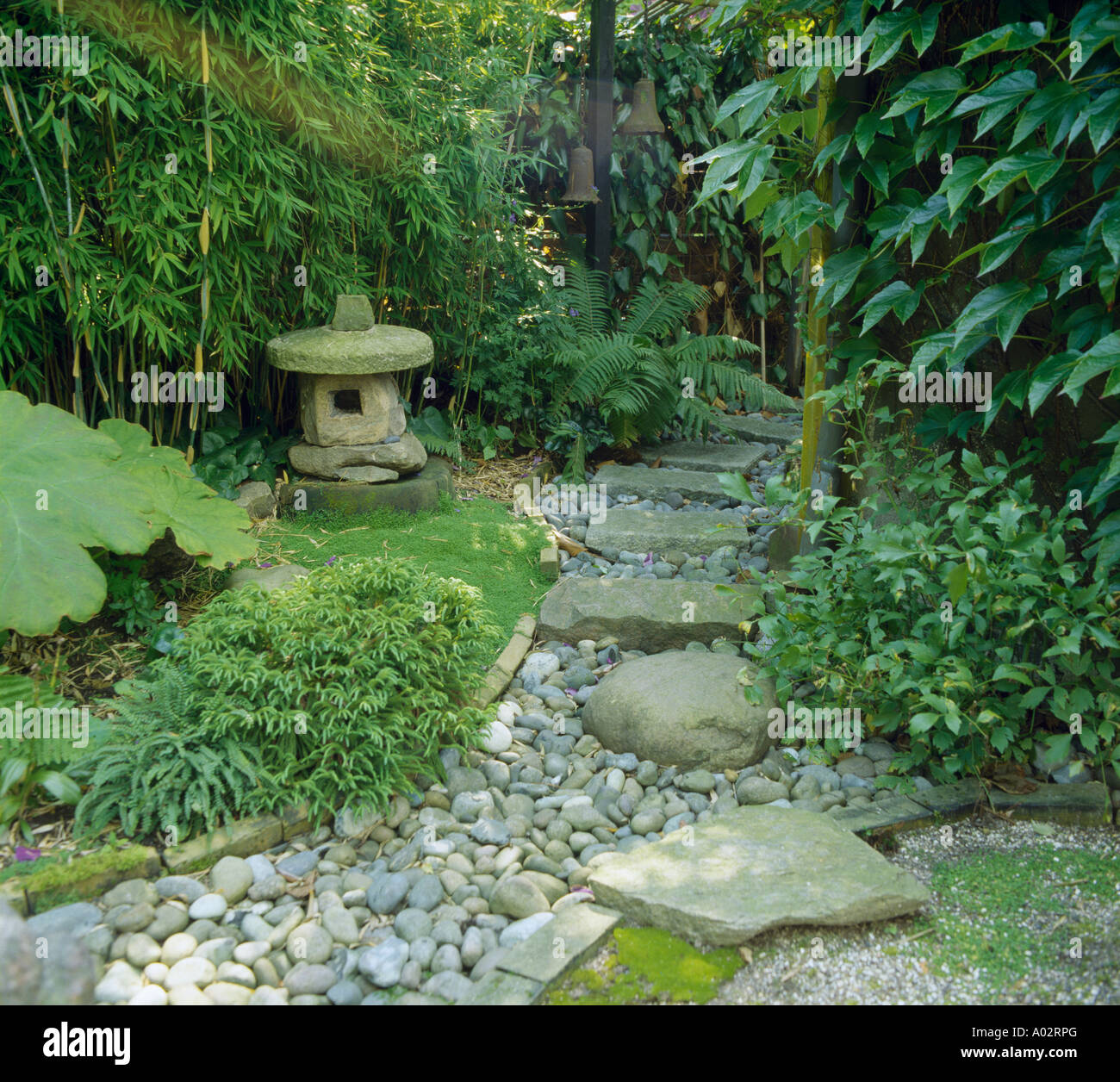 Di ghiaia e di pietra percorso tra arbusti e Arundinaria con pietra lanterna orientale scultura in stile Giapponese a giardino Foto Stock