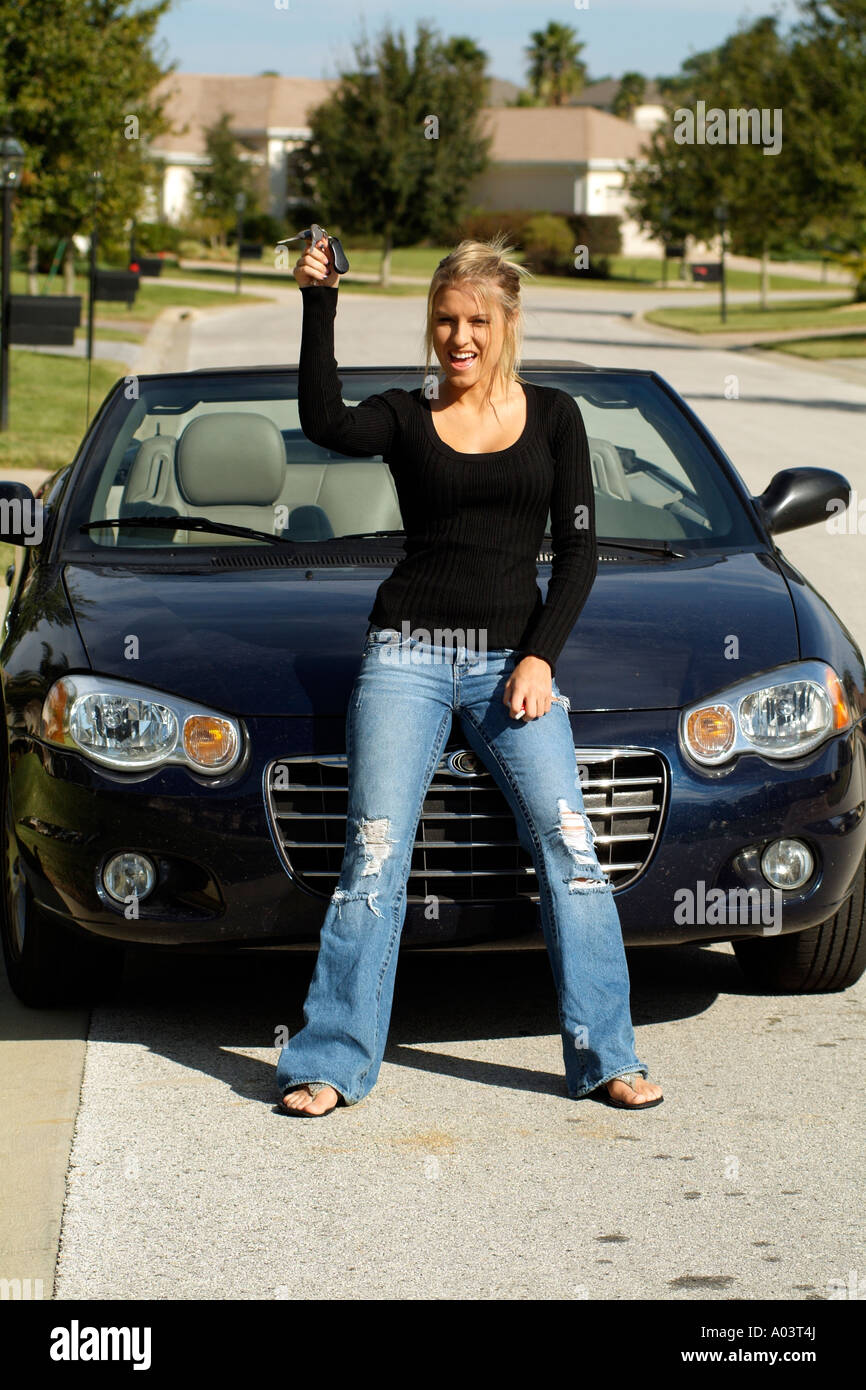 Giovane ragazza che indossa jeans tenendo premuto i tasti con un blu auto sportiva Foto Stock