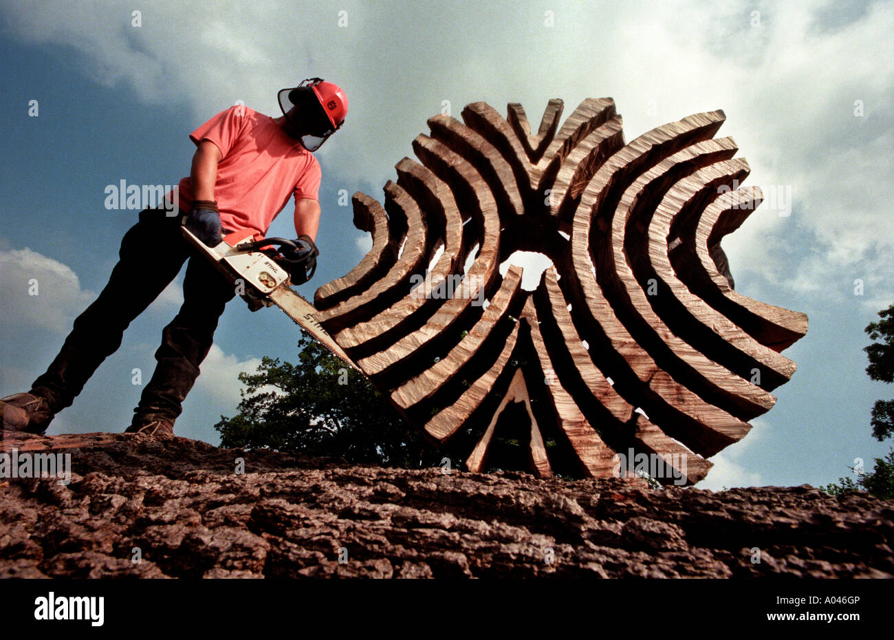 Legno riciclato di essere trasformato in una scultura da uomo in elmetto con chainsaw. Foto Stock