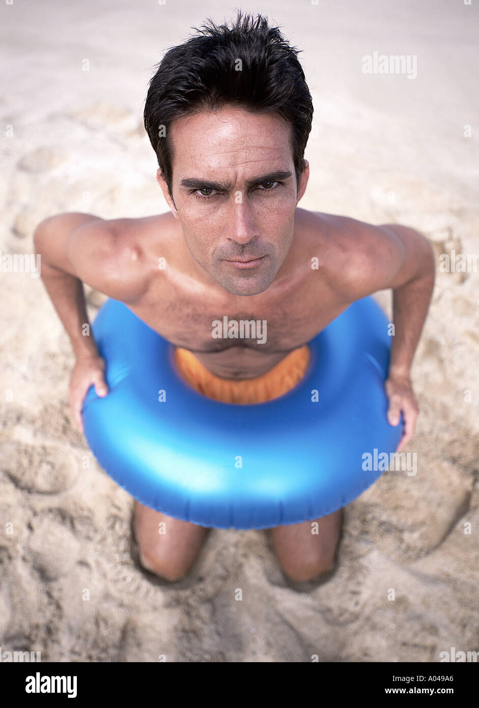 Ritratto di un giovane uomo che indossa un gonfiabile blu anello in gomma intorno alla vita Inginocchiati sulla spiaggia Foto Stock