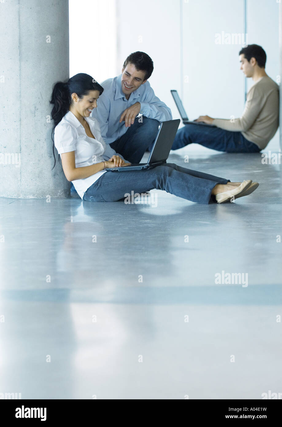 L uomo e la donna sul piano, utilizzando laptop e parlare, secondo uomo in background Foto Stock
