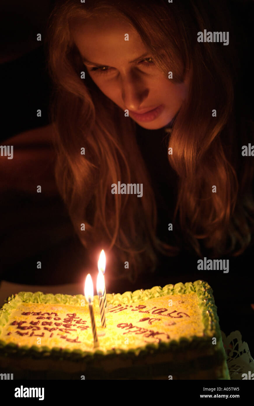 Womans viso illuminato da candele su una torta di compleanno Foto Stock
