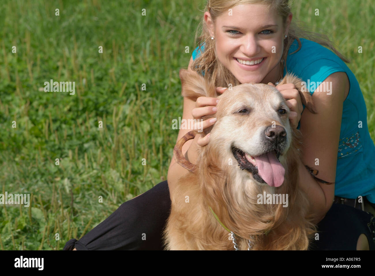 Una donna bionda tenendo le orecchie del suo cane sorride alla telecamera Foto Stock