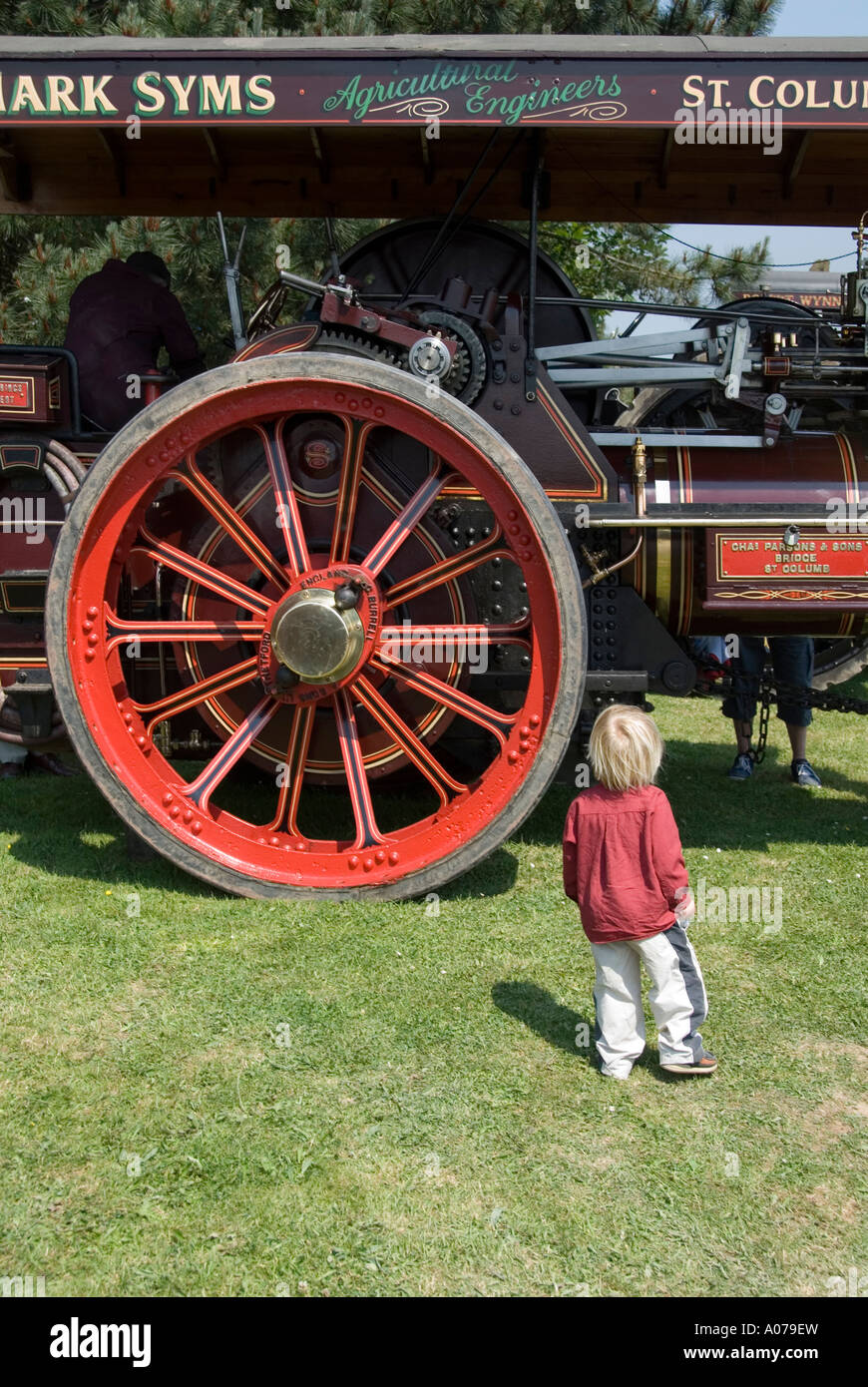 Il bambino "moderno" si trova di fronte alla grande ruota sull'antico motore a vapore al Royal Cornwall Agricultural Show di Wadebridge, Inghilterra, Regno Unito Foto Stock