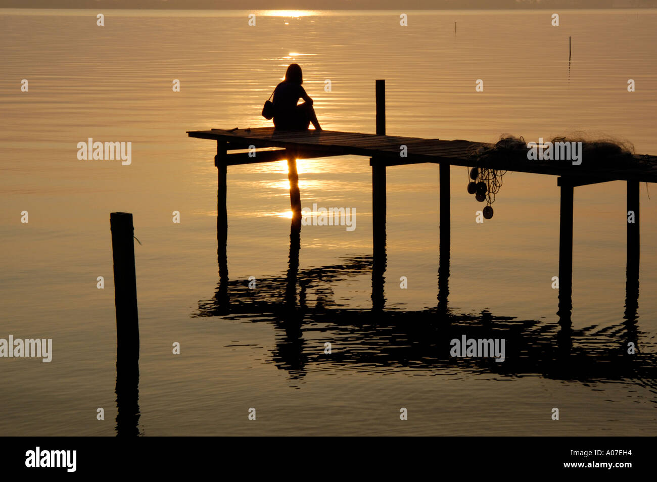 Silhouette di donna e pier con oro rame luce che riflette da acqua liscia Foto Stock