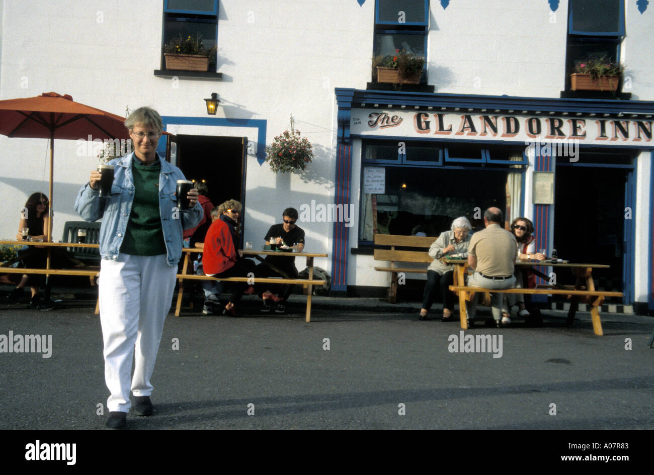 Persone mangiare e bere donna portante due pinte di fronte al Glandore Inn Glandore nella contea di Cork in Irlanda Foto Stock