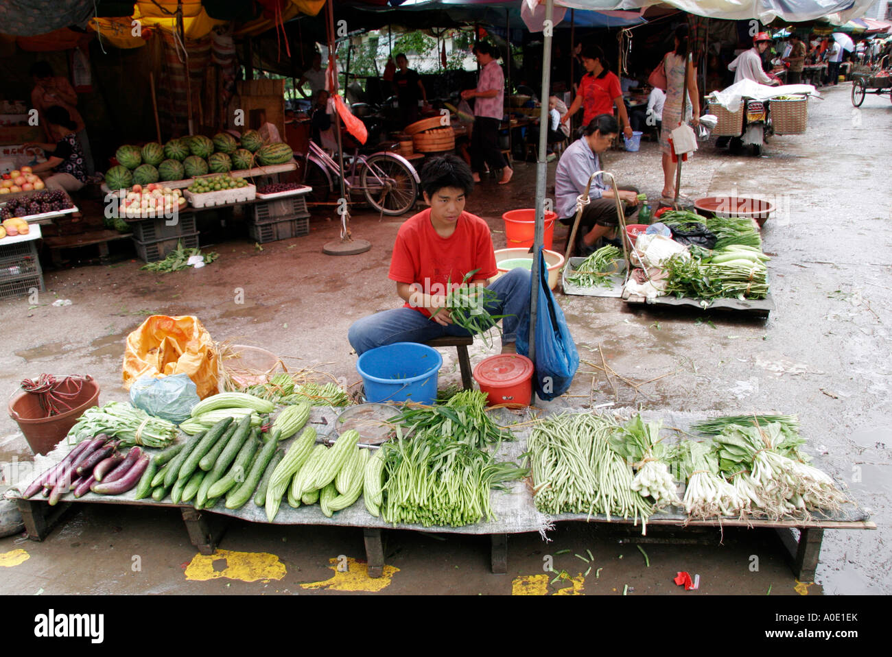 Ragazzo in un rosso Tshirt frequentando il suo stallo vegetale nel mercato di Yangshuo, a sud-ovest della Cina. Foto Stock
