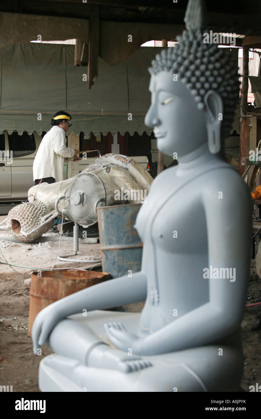 Sullo sfondo un uomo sta lavorando su Buddha in bronzo in primo piano vi è una fresca casted Buddha a la fusione in bronzo in officina Phitsanoluk Foto Stock