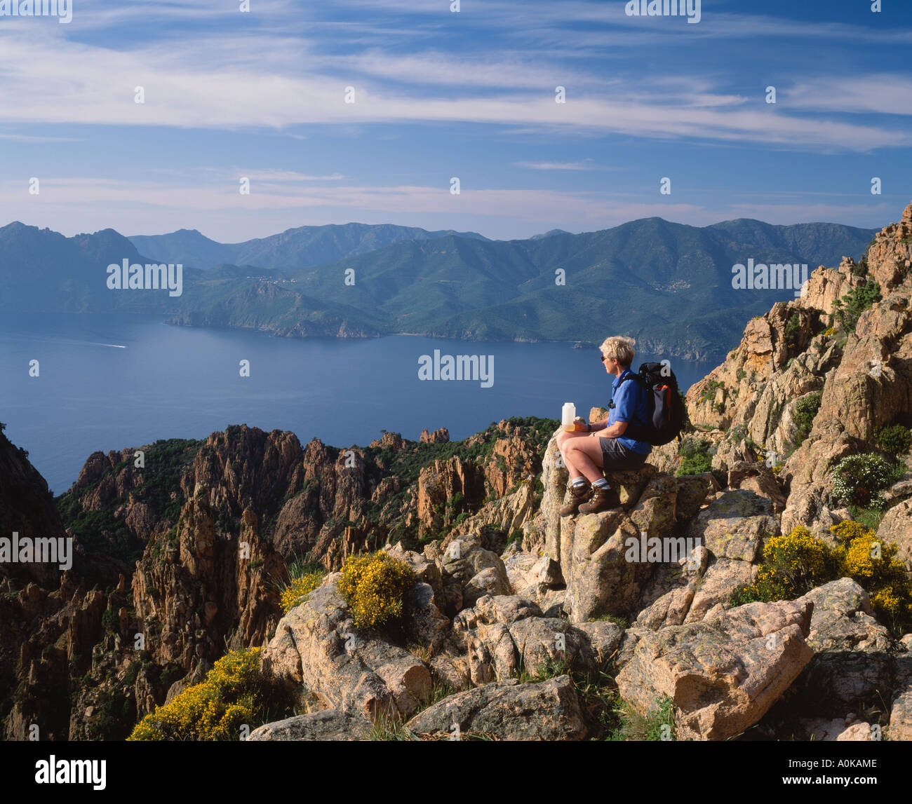Il camminatore femmina seduta sulle rocce, le Calanche al di sopra del Golfe de Porto, Corse du Sud, Corsica, Francia. Patrimonio mondiale dell UNESCO Foto Stock